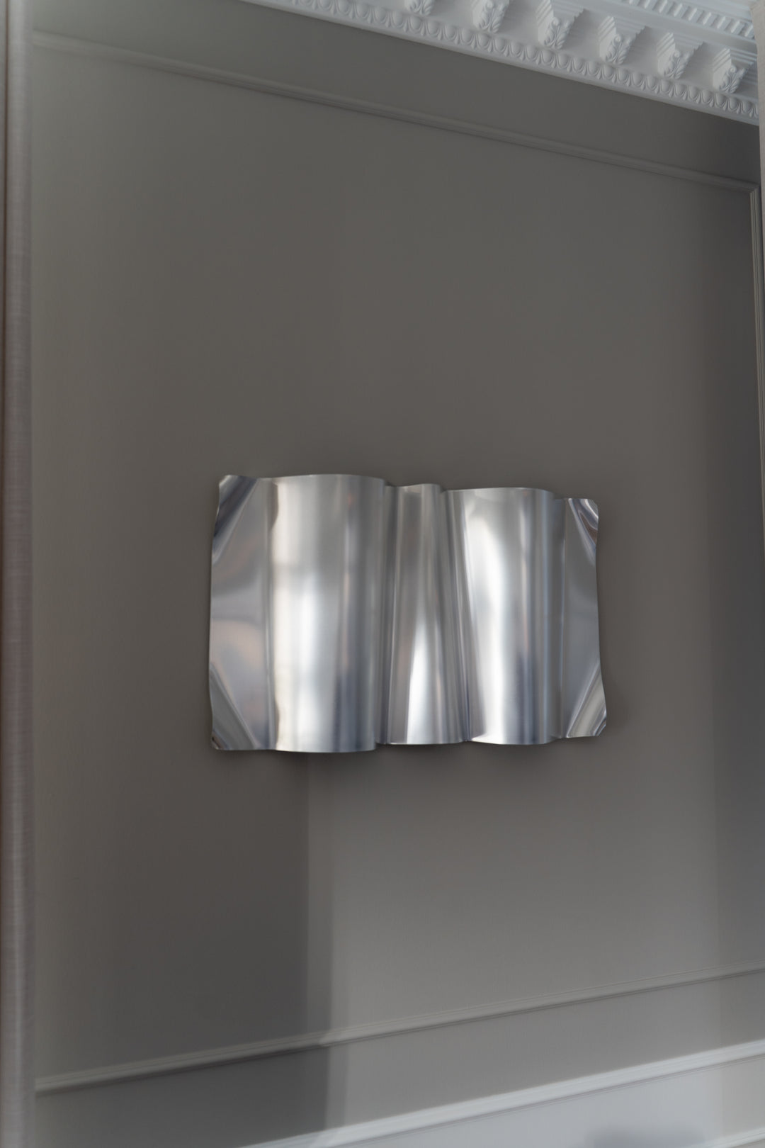 Modern sculpural metal wall art with wavy design on a gray wall