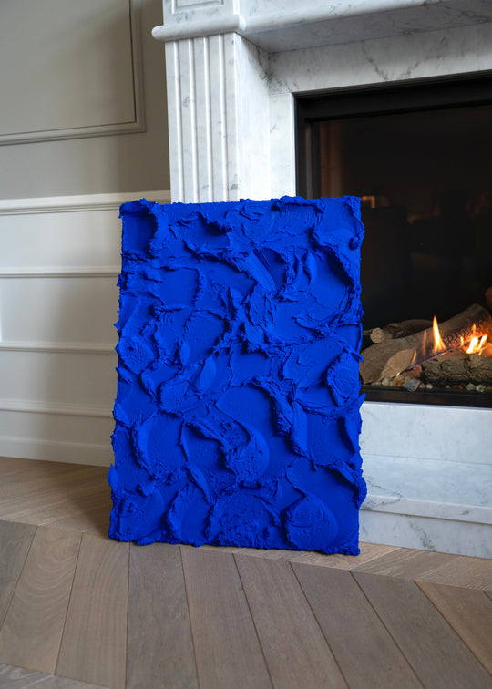 Blue textured artwork in front of a fireplace. Kunst fra Iværksætter-TV.